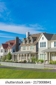 Vertical White Clouds Neighborhood Houses With Gable Roof And Front Porches At Daybreak, Utah. Exterior Of Large Houses With White Picket Fences And Paved Side Walk Near The Large Green Field