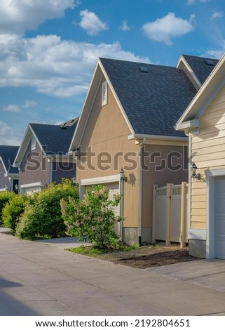 Vertical White puffy clouds Attached garages at the back of the houses at Daybreak, Utah. Garages' exterior with gable roofs, white garage doors and concrete driveways.