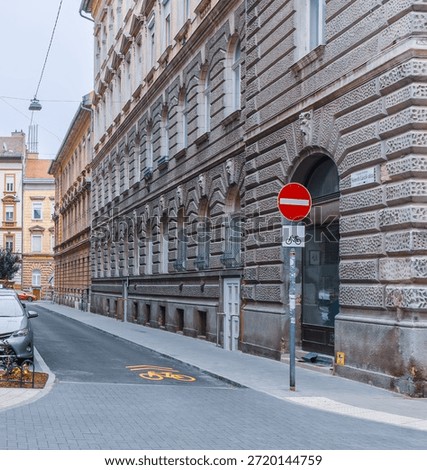 Vertical wide angle eye level shot of a narrow Budapest street featuring a yellow bicycle lane marking, a no-entry sign, and classic stone facades