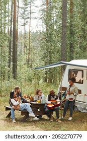 Vertical Wide Angle View At Diverse Group Of Young People Enjoying Picnic Outdoors While Camping With Trailer Van, Copy Space