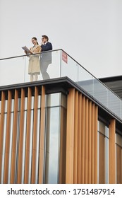 Vertical Wide Angle View At Two Business People Reading Contract While Standing On Roof Of Office Building With For Rent Sign, Copy Space