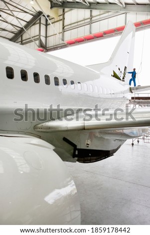 Vertical wide shot of an engineer assembling the tail of a passenger jet at a hangar.