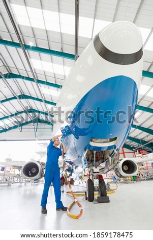 Vertical wide shot of an engineer working on a passenger jet in a hangar.