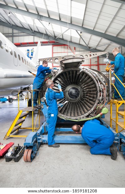 Vertical wide shot of engineers assembling an\
engine of a passenger jet at a\
hangar.