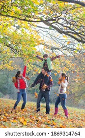 Vertical Wide Shot Of A Family Playing With Dry Leaves In An Autumnal Park.