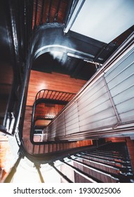 A vertical wide-angle view of an antique wooden indoor stairwell going down by spiral to the entrance, with a built-in metal case of the lift shaft connecting the building floors