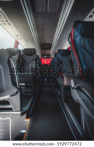 A vertical wide-angle view of an empty interior of a regular intercity bus with rows of leather numbered seats with red borders, carpeted seat aisle in the center