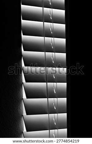 Vertical window blinds filter dim light into a dark interior, creating narrow shadows that reflect nightshift fatigue, isolation, and quiet depressive stillness.