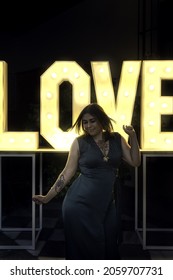 A  Vertical Of A Young Spanish Girl Standing In Front Of The Illuminated Word Love