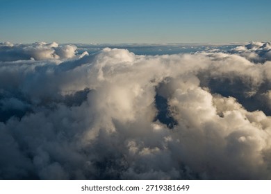 vertically developing white and grey cumulonimbus clouds see from above under a clear blue sky with sunlight