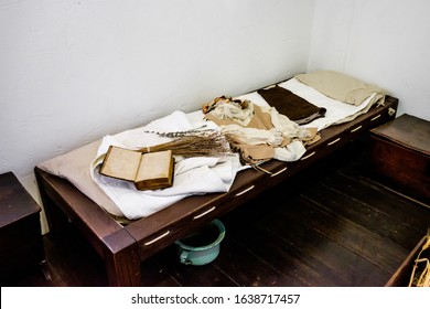 Very Antique, Messy, And Dirty Bedroom With Weathered Books, Clothes, Wooden Furnitures And White Walls