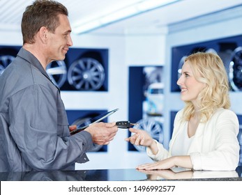 A Very Attractive Young Blonde Women Get Her Car Keys Back At The Counter Of The Tire And Car Service Workshop From The Mechanical Employee Of The Succesfull Service And Looks Very Satisfied And Happy