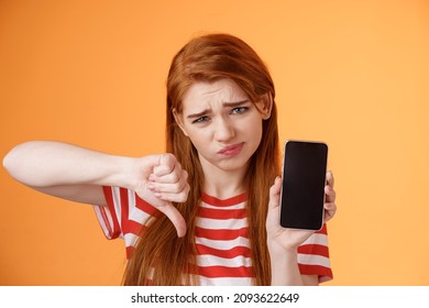 Very Bad Poor Quality. Upset Redhead Female Customer Grimace Disappointed, Show Smartphone Blank Display, Thumbs Down Judgement, Dislike App, Smirk Dismay, Stand Upset Orange Background