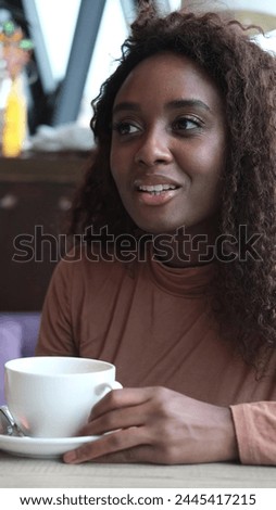 A very beautiful African American woman is sitting at a table in a cafe with a cup of coffee or tea. Stock photo © 