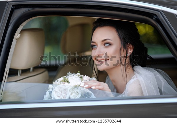 Very beautiful  bride jewelry head sits in a black\
car on your wedding day with a bouquet. Portrait of the bride.\
fluffy white lace dress