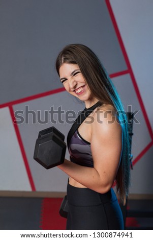 Very beautiful girl trains biceps with dumbbells in the gym.