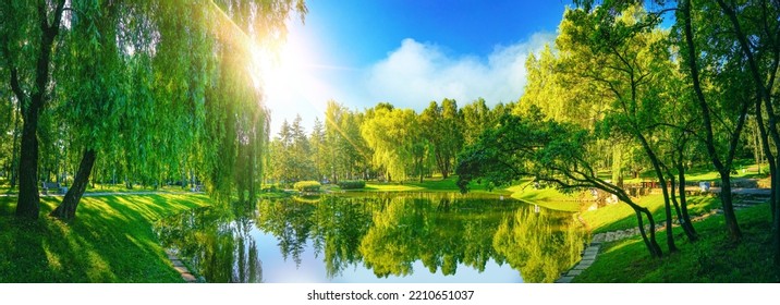 Very beautiful idyllic natural panorama of city spring summer park with pond that reflects surrounding trees and blue sky on bright sunny day.
