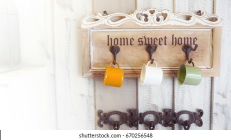 Very bright shot of three colored mugs hanging on hooks of wooden board decorated on classic wall, with copy space on left, giving feeling of being cozy at home 