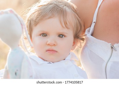 A Very Close Up Portrait Of A Little Girl With Brown Eyes Of A Blonde, Curly Hair, Looking Seriously At The Camera, Not Smiling. The Knowledge Of Exploring The World, Walking On The Street With Parent