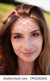 A very close-up portrait of a young woman with sunny face shadows from a straw hat. Natural beauty without makeup. Clean skin, face care. Expressive, large brown eyes