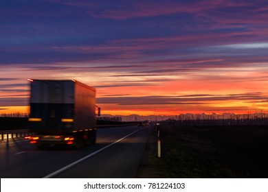 A very colorful sunset and a moving (blurred) truck on an asphalt road
