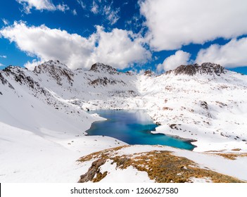 A very deep blue lake sits in a valley between snow capped mountains on a partly cloudy day - Powered by Shutterstock