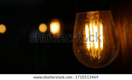 Very detailed macro of an Edison bulb with yellow light bokeh in the dark background.