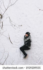 A Very Drunk Homeless Man In A Black Coat Lies Sleeping On His Side On White Snow In A Cold Frosty Winter With A Bottle Of Alcohol. Photography, Concept, Copy Space.