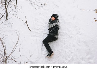 A Very Drunk Homeless Man In A Black Coat Lies Sleeping On His Side On White Snow In A Cold Frosty Winter With A Bottle Of Alcohol. Photography, Concept, Copy Space.