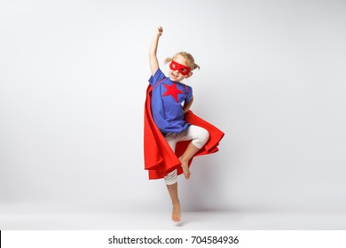 Very excited little girl dressed like superhero jumping alongside the white wall.