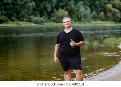very fat guy drinks water after training in the park in summer
