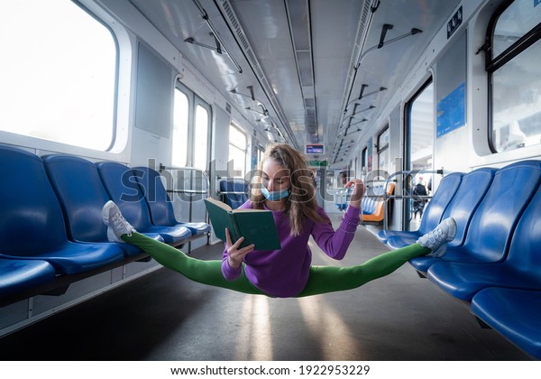 Very flexible wearing mask woman reading book in\
the subway car sitting in the gymnastic split. Concept of healthy\
lifestyle, flexibility and\
yoga
