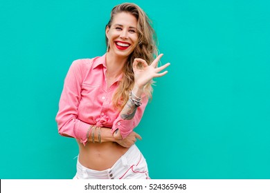 Very Good! Young Pretty Smiling Woman Showing OK Sign Against Green Wall.