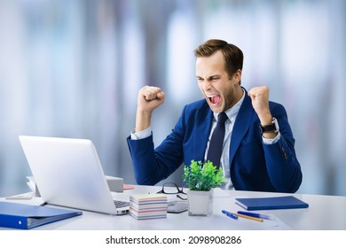 Very Happy Businessman In Blue Suit, Working With Laptop Computer At Office. Excited Business Man Rising Hands Up With Clenching Fists - Success In Job Education Concept. Skype Zoom Video Conference.