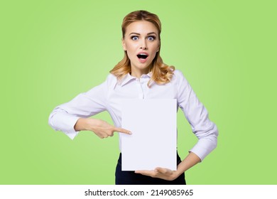 Very happy, excited surprised, astonished businesswoman with wide opened eyes, mouth, show blank paper signboard. Success in business concept. Copy space place for text. Green background. Astonishment