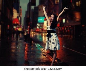 Very Happy Female Walking In A NYC Street With Her Hands Rised. Perfect Lovely Charming  Lady Rising Her Hands In New York City On Wet Pavement With Ad Reflections. NYC In A Night Time.Adventure Time!