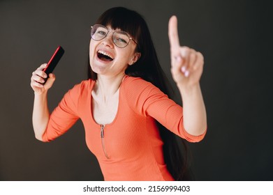 A Very Happy Girl In Glasses Is Talking On The Phone On A Black Plain Background. Happy Day Of The Year Concept