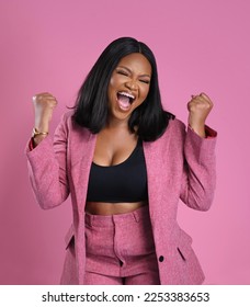 Very Happy and joyful African American woman makes victory dance, raises clenches fists and lifts up from joy, rejoicing triumph feeling winner, smiles broadly, on pink background. - Shutterstock ID 2253383653
