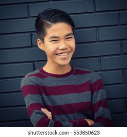 Very happy teenage Asian boy with braces smiling with arms folded in front.
