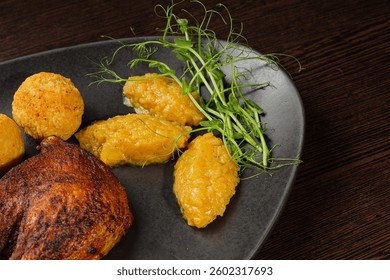 Very healthy roast duck thigh with potatoes and greens on a black plate on a wooden table serving in a restaurant. nice decoration of the dish. medium plan of greenery