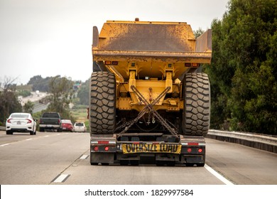 A very large haul dump truck being hauled by an 18 wheel truck down a freeway