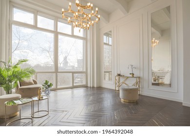 very light and bright interior of luxurious cozy living room with chic soft beige furniture with gold metallic elements, huge window to the floor and wooden parquet