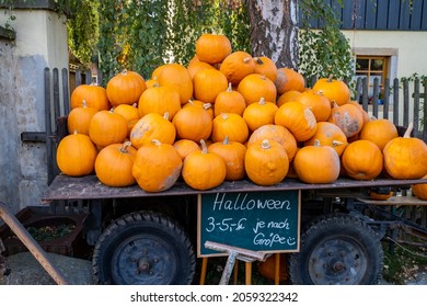 Very Many Pumpkins Are On A Trailer For Sale. Different Size Pumpkins For Halloween To Take Home. On A Small Black Board Is The Price. 