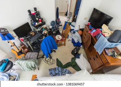 Very Messy, Cluttered Suburban Teenage Boys Bedroom With Piles Of Clothes, Music And Sports Equipment.  