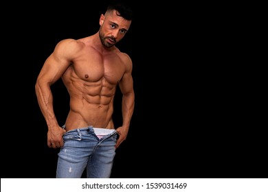 Very muscular fitness model man, posing dressed in jeans and no shirt. there is a black background - Powered by Shutterstock