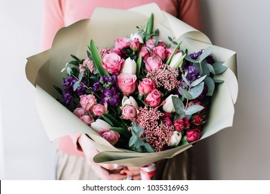 Very nice florist woman holding a beautiful colourful blossoming flowers bouquet of fresh roses, carnations, tulips, eucalyptus on the grey wall background