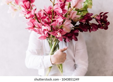 Very Nice Young Man In A White Shirt Holding A Huge Bunch Of Cymbidium Orchid Flowers, Covering His Face 