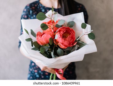 Very Nice Young Woman Holding Beautiful Blossoming Flower Bouquet Of Three Giant Fresh Coral Coloured Peonies And Eucalyptus On The Grey Background