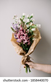 Very nice young woman holding big and beautiful bouquet of fresh campanula, delphinium and snapdragon flowers in white, pink and purple colors, cropped photo, bouquet close up