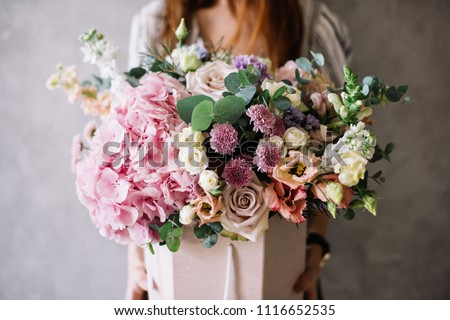 Very nice young woman holding beautiful tender blossoming bouquet of fresh hydrangea, eustoma, roses, eucalyptus flowers in pastel pink and cream colours on the grey wall background